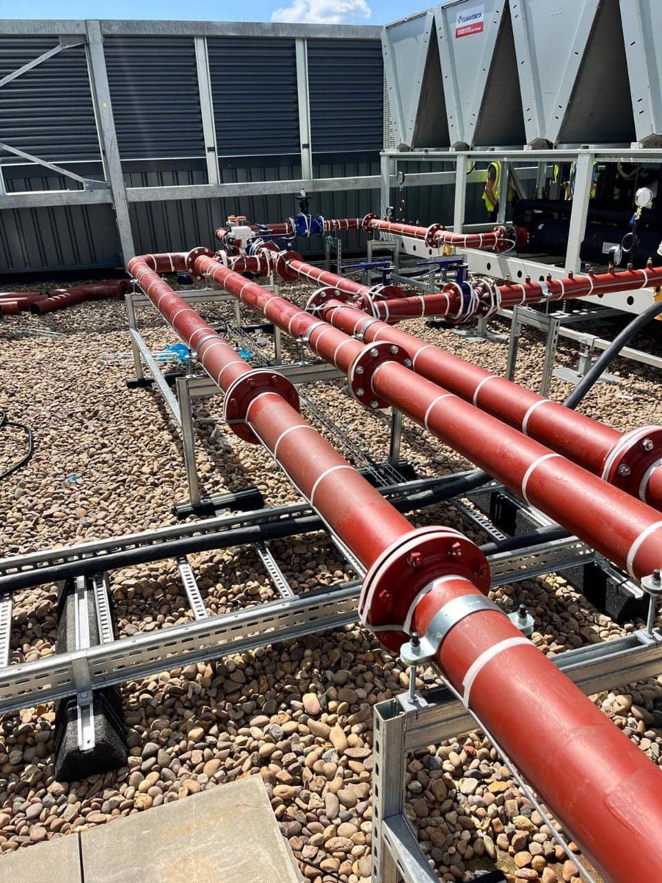 Red insulated trace-heated pipework, valves and chillers on a rooftop plant installation